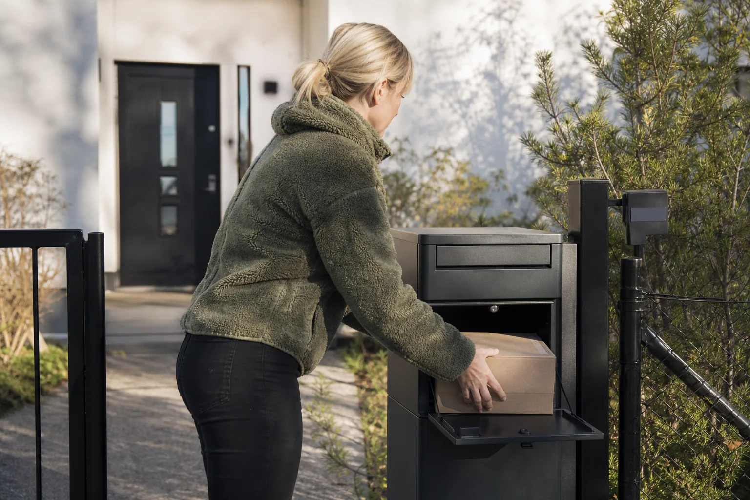 Person hämtar ett paket genom en bakre lucka på en paketpostlåda från gårdssidan